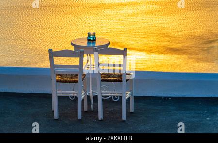 Zwei Stühle und ein kleiner Tisch mit Blick auf den dramatischen Sonnenuntergang in Santorin in Griechenland. Stockfoto
