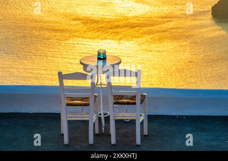 Zwei Stühle und ein kleiner Tisch mit Blick auf den dramatischen Sonnenuntergang in Santorin in Griechenland. Stockfoto