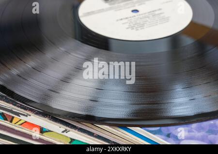 Nahaufnahme einer schwarzen Schallplatte mit Rillen, die auf einem Stapel anderer Schallplatten ruht. Stockfoto