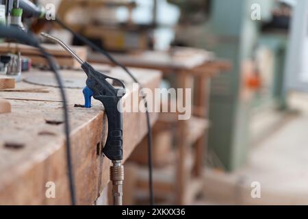 Luftstaubgerät liegt auf einer Werkbank in einer Tischlerei, andere Werkzeuge und Maschinen im Hintergrund sind unscharf. Das Bild vermittelt einen Sinn Stockfoto