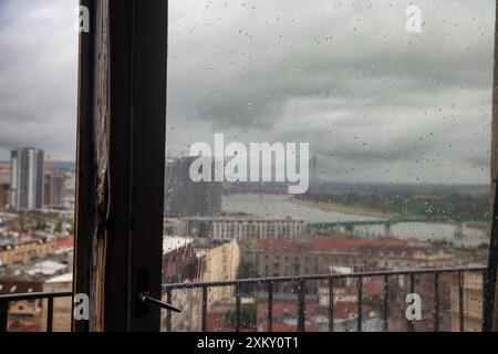 Der Blick auf Belgrad von zu Hause aus durch ein von Regentropfen gewaschenes altes Holzfenster bietet an einem regnerischen Tag eine charmante und nostalgische Stadtlandschaft Stockfoto