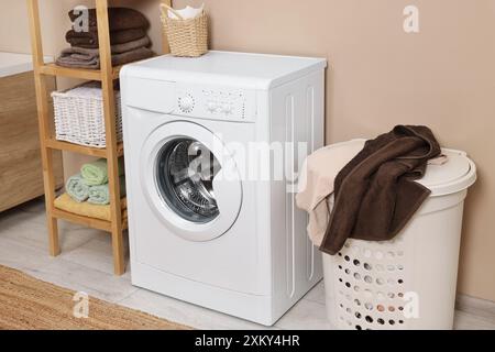 Waschmaschine, Korb und Regal in der Nähe beigefarbener Wände im Innenbereich Stockfoto