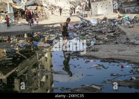 Gaza. Juli 2024. Menschen laufen zwischen Trümmern und Abwasserpfützen im Flüchtlingslager Jabalia im nördlichen Gazastreifen, 24. Juli 2024. Der Nachweis von Poliovirus Typ 2 (VDPV2) in Abwasserproben aus dem Gazastreifen wurde in Tests in Israel gefunden, sagte das israelische Gesundheitsministerium in einer Erklärung vom 18. Juli. Quelle: Mahmoud Zaki/Xinhua/Alamy Live News Stockfoto