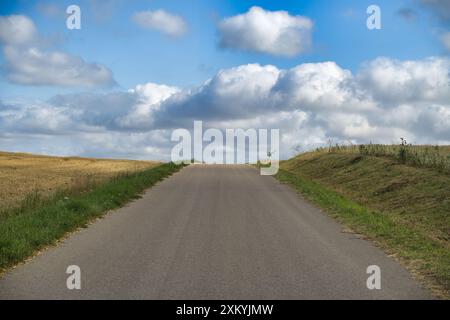 Leere Landstraße, die sich an einem sonnigen Tag mit blauem Himmel und verstreuten Wolken zum Horizont hin erstreckt. Stockfoto