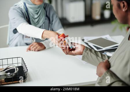 Hand eines jungen weiblichen Arztes, der eine Flasche Pillen an schwangere afroamerikanische Patientin über den Schreibtisch übergibt, nachdem er Ratschläge über die Einnahme von Medikamenten gegeben hat Stockfoto