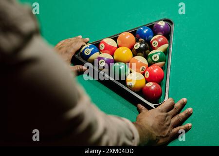 Hoher Handwinkel eines jungen, nicht erkennbaren Mannes, der vor grünem Billardtisch steht und dreieckige Gestelle mit Kugeln berührt Stockfoto