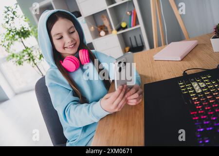 Foto eines fröhlichen süßen liebenswerten Mädchens, das Gadgets, moderne Technologie im Haus benutzt Stockfoto