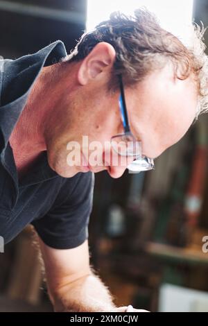 Fokussierter Zimmermann arbeitet an einem Holzprojekt in einer gemütlichen Werkstatt, umgeben von Werkzeugen und Sägemehl. Seine Leidenschaft und sein Fachwissen zeigen sich im Detail seines han Stockfoto