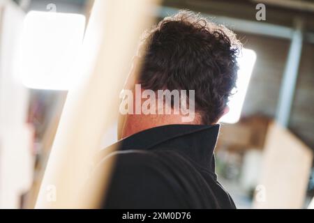 Zimmermann konzentriert sich auf ein Holzbearbeitungsprojekt in seiner Werkstatt. Umgeben von Werkzeugen und Holz. Das helle Licht des Fensters leuchtet auf Stockfoto