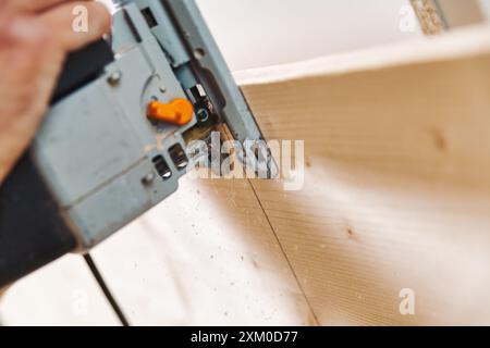 Erfahrener Zimmermann mit Stichsäge, um Holz in der Werkstatt zu schneiden und handgefertigte Stücke mit Präzision und Einsatz zu kreieren. Sägemehl verleiht dem Bild Authentizität Stockfoto