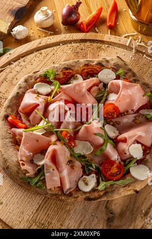 Appetitliche hausgemachte Pizza mit Mortadella, Aradel, Tomaten und Mozzarella auf einem Holzbrett Stockfoto