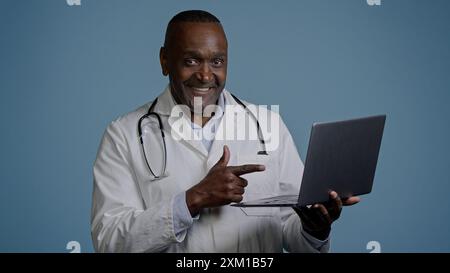 afroamerikaner Mann Arzt Therapeut ethnischer männlicher Chirurg in weißem Mantel im blauen Hintergrund Studio, das auf Laptop-Beratung Patient online Remote arbeitet Stockfoto