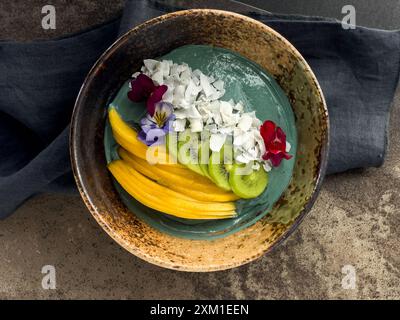 Spirulina Smoothie Schüssel mit Mango Kiwi und Kokosflocken, wunderschön dekoriert. Stockfoto