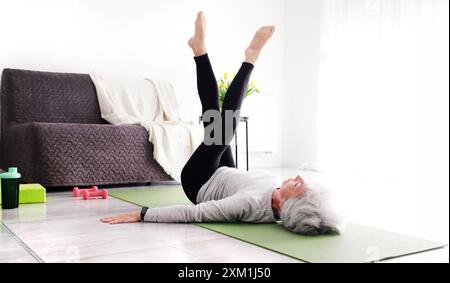 Ältere Frau Mit Grauem Haar Zu Hause Macht Yoga Und Dehnübungen, Sieht Attraktiv Aus Stockfoto