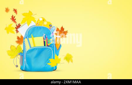 Blauer Rucksack mit Schulsachen und fliegenden Herbstblättern auf gelbem Hintergrund. Kopierbereich Stockfoto