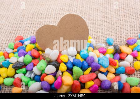 Herz aus Papier inmitten der bunten Steinchen auf Leinwand Boden Stockfoto