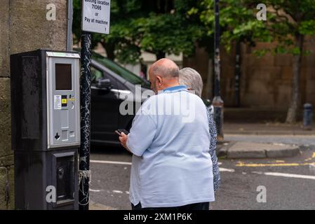 Ein Foto eines älteren Ehepaares, das eine kontaktlose Parkmaschine benutzt, um ihre Verwirrung festzuhalten, während sie versuchen, die Technologie herauszufinden. Dieses ehrliche Bild Stockfoto