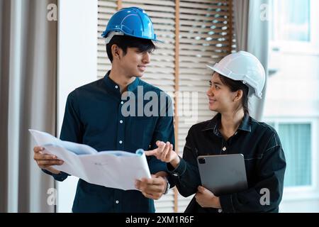 Zwei Ingenieure diskutieren Blueprint- und Projektpläne auf einer Baustelle mit Schutzhelmen Stockfoto