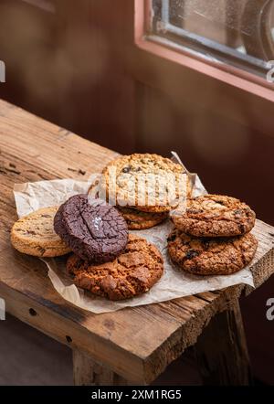 Handgemachte, gemischte Kekse, Schokoladen-Chip-Kekse und Haferkekse auf Pergamentpapier. Holztisch. Draufsicht. Stockfoto