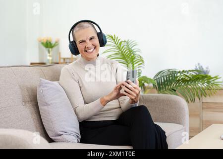 Entspannte, reife Frau aus den 60er Jahren, ältere Kundin mittleren Alters, die ihr Smartphone über die mobile App hält, SMS schickt Stockfoto