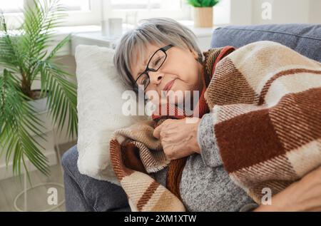 Ältere Frau, die zu Hause auf dem Sofa liegt, in eine Decke gewickelt und sich ungesund mit Grippe fühlt Stockfoto