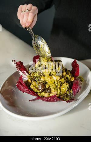 Frauenhände gießen Gemüse auf den Teller. Grüner Salat. Veganes, vegetarisches Essen. Stockfoto