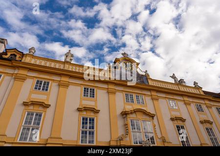 Melk, Österreich - 25. Oktober 2023 : Ein gelbes Gebäude mit Uhrenturm und Skulpturen vor bewölktem Himmel in Melk, Österreich. Stockfoto