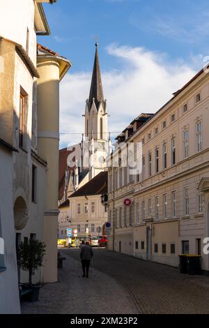 Melk, Österreich - 25. Oktober 2023 : Eine Kopfsteinpflasterstraße in Melk, Österreich, mit einem hohen Kirchturm im Hintergrund. Stockfoto