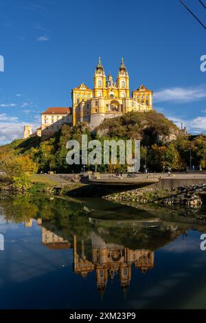 Melk, Österreich - 25. Oktober 2023 : auf einem Hügel befindet sich Ein gelb-weißes Gebäude, das sich in einem ruhigen Gewässer spiegelt. Bäume umgeben das Gebäude Stockfoto