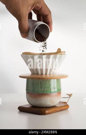 Eine zarte Hand kaskadiert feinen Kaffeesatz in den makellosen Papierfilter und verspricht eine aromatische Infusion. Stockfoto