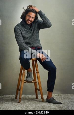 Stuhl, Mann und Lächeln für Mode im Studio auf grauem Hintergrund mit Bürokleidung. Männlicher Mensch, Porträt und glücklich oder zufrieden mit eleganter Kleidung Stockfoto