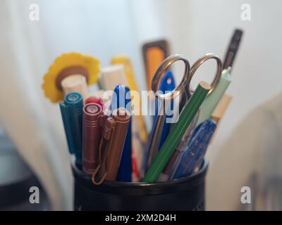 Nahaufnahme verschiedener Stifte, Marker und Scheren in einem schwarzen Halter auf einem Schreibtisch Stockfoto