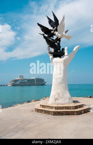 Aydin Kusadasi, Türkei - 4. Juli 2024: Hand des Friedens Skulptur und Kreuzfahrtschiff dahinter in Kusadasi Aydin Stockfoto