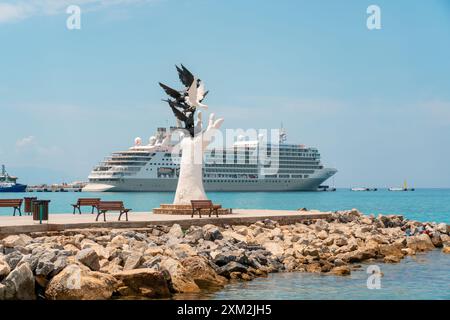 Aydin Kusadasi, Türkei - 4. Juli 2024: Hand des Friedens Skulptur und Kreuzfahrtschiff dahinter in Kusadasi Aydin Stockfoto