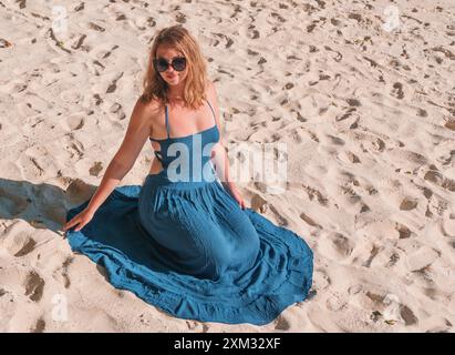 Frau in blauem Kleid, die auf weißem Sandstrand sitzt Stockfoto