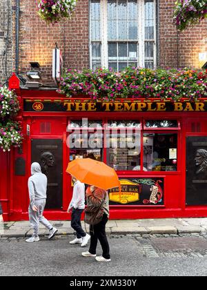 Leute, die an einem regnerischen Tag am Temple Bar Pub in Dublin, Irland, mit einem orangefarbenen Regenschirm vorbeilaufen Stockfoto