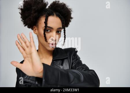 Eine junge Afroamerikanerin in einer schwarzen Lederjacke posiert vor grauem Hintergrund. Stockfoto