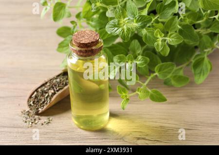 Ätherisches Öl in der Flasche, Löffel mit trockenem Kraut und Oregano-Blättern auf Holztisch, Nahaufnahme Stockfoto