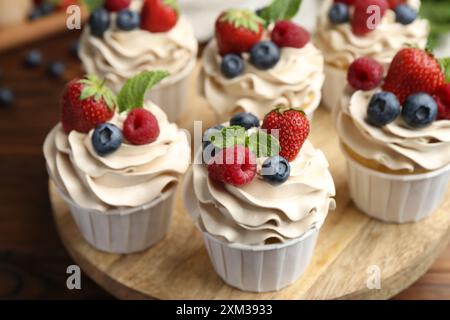 Leckere Cupcakes mit verschiedenen Beeren und Minze auf Holztisch, Nahaufnahme Stockfoto