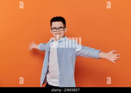 Junge mit Down-Syndrom, Arme ausgestreckt vor orangem Hintergrund. Stockfoto