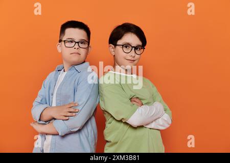 Zwei Jungen, einer mit Down-Syndrom, stehen nebeneinander vor einem orangefarbenen Hintergrund. Stockfoto