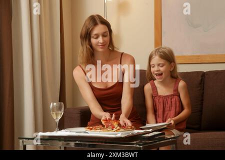 Eine junge Frau genießt Pizza mit ihrer kleinen Tochter im Wohnzimmer Stockfoto