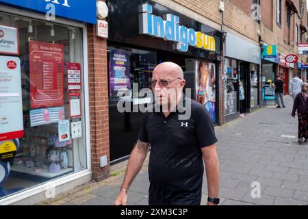 Die Menschen kommen am 25. Juli 2024 in Birmingham, Großbritannien, am Indigo Sun Sonnenbad auf der Kings Heath High Street vorbei. Kings Heath ist ein Vorort im Süden von Birmingham, 6 km vom Stadtzentrum entfernt und das nächste Viertel südlich von Moseley an der A435 Alcester Road. Das Einkaufsviertel verläuft entlang der High Street mit Geschäften, darunter Filialen von nationalen Filialen, unabhängigen Geschäften, Wohltätigkeits- und Schnäppchenläden, Supermärkten und Bekleidungshändlern. Stockfoto