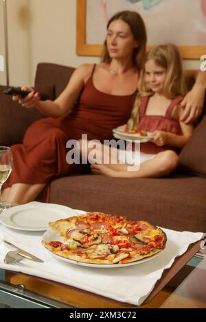 Eine junge Frau genießt Pizza mit ihrer kleinen Tochter im Wohnzimmer Stockfoto