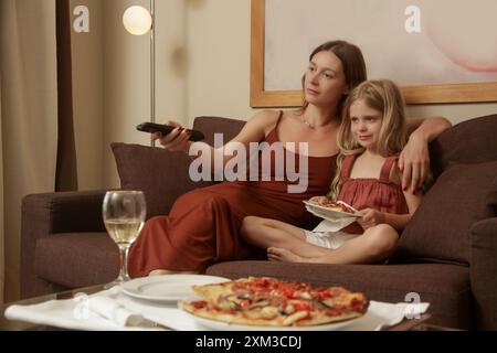 Eine junge Frau genießt Pizza mit ihrer kleinen Tochter im Wohnzimmer Stockfoto