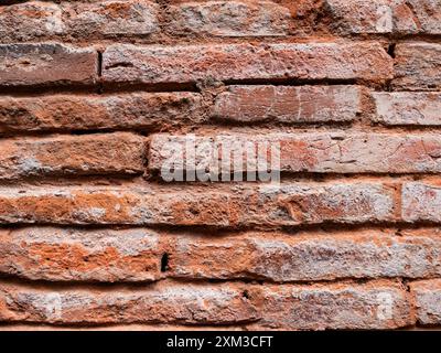 Eine Nahaufnahme einer verwitterten roten Ziegelmauer mit horizontal verlegten Ziegelreihen. Stockfoto