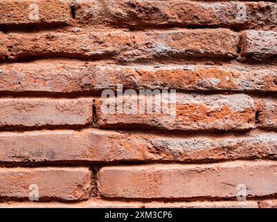 Eine Nahaufnahme einer verwitterten roten Ziegelmauer mit horizontal verlegten Ziegelreihen. Stockfoto