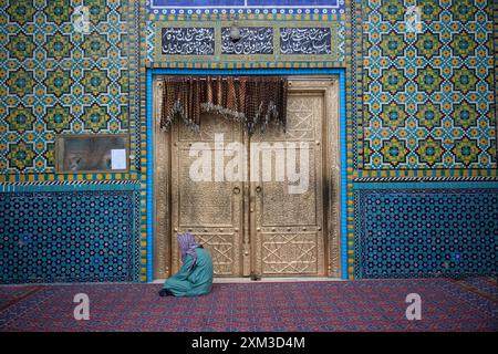 Ein Mann sitzt im Gebet am Eingang des Schreins von Hazrat Ali, auch bekannt als Blaue Moschee, in Mazar-i-Sharif, Nordafghanistan. Stockfoto