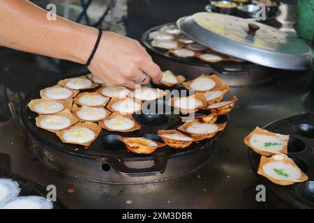 Der Verkäufer nimmt Kanom Krok, beliebte thailändische Kokosnussmilchpfannkuchen, aus der Pfanne, wenn sie zum Servieren bereit sind Stockfoto