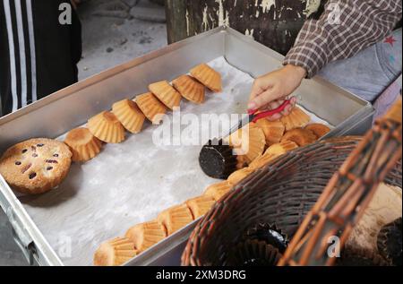 Baker entfernt frisch gebackene Khanom Farang Kudeejeen-Kuchen aus den Formen, einem berühmten portugiesisch beeinflussten Cupcake in Thailand Stockfoto